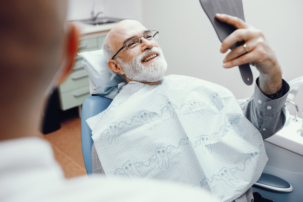 Dental technology is used for an older gentleman who's admiring his smile in a handheld mirror.