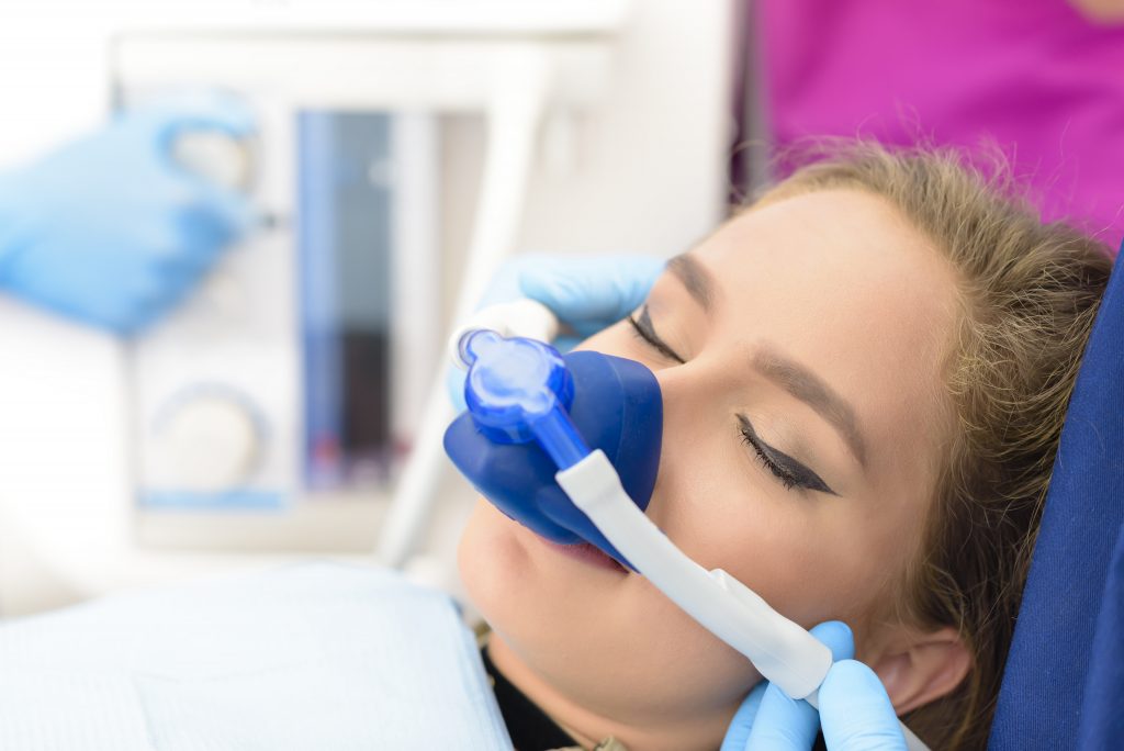 A woman with winged eyeliner is wearing a mask and is having sedation dentistry administered.