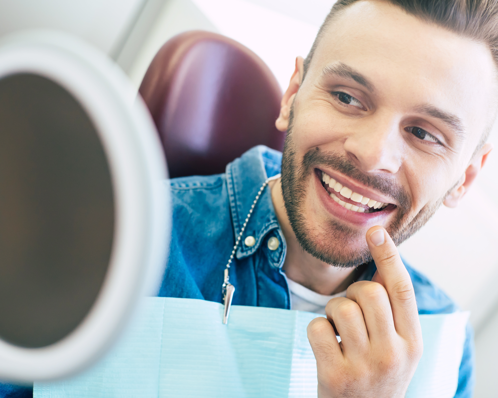 man looking at teeth in mirror